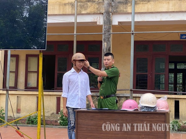 Cán bộ Công an xã hướng dẫn học sinh cách đội mũ bảo hiểm an toàn