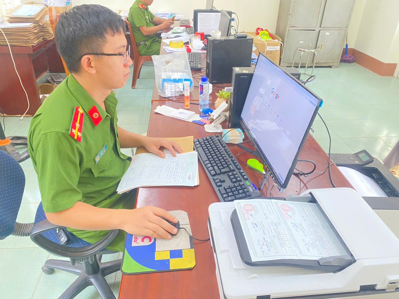A person in uniform sitting at a desk with a computerDescription automatically generated