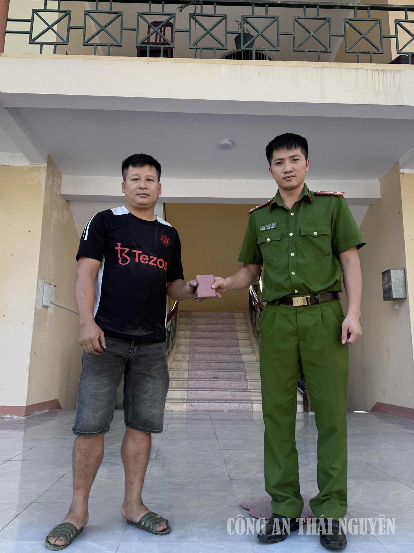 Anh Hoàng Hữu Tài (bên trái) giao nộp chiếc ví nhặt được cho Công an xã Thần Sa